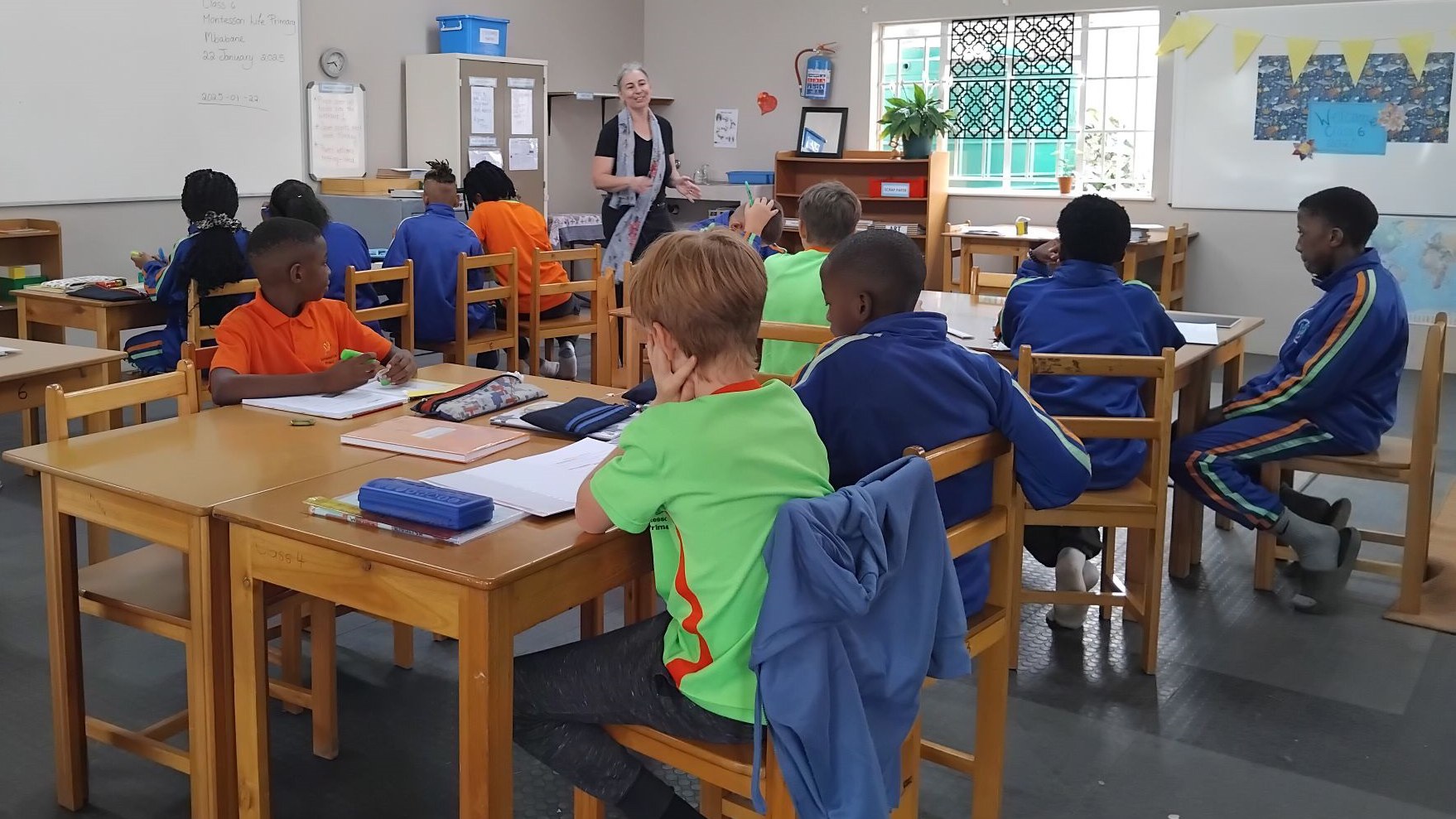 A sense of order and concentration in the classroom. Students work diligently at their desks, engaging in focused, individualised learning, while the teacher presents a lesson.